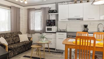 A compact living space with a sofa, a dining table with chairs, a kitchen area with appliances, and a television.