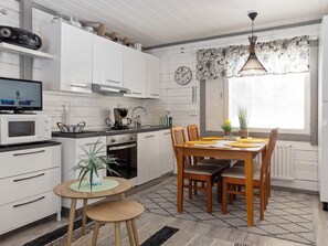 A modern kitchen with white cabinets, a microwave, a coffee maker, and a dining area with a wooden table and chairs. - Vacation home Riekko by Interhome (Enontekiö)