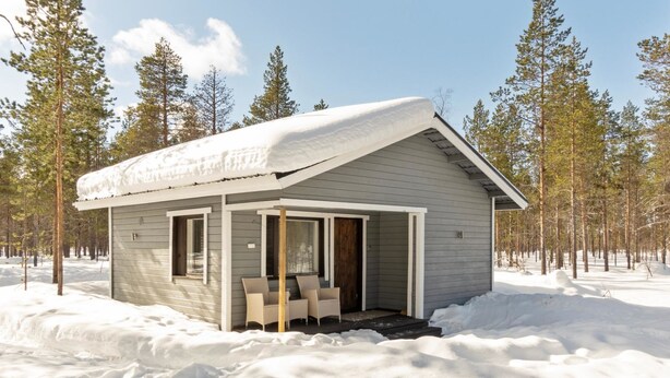 Eine kleine Holzhütte mit Veranda, umgeben von Schnee und Bäumen.