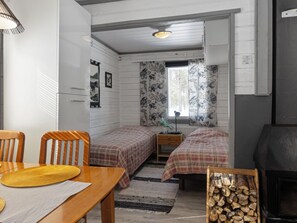 A compact room with two beds, a wooden table with a yellow placemat, a small bedside table, a radiator, and a fireplace. - Vacation home Riekko by Interhome (Enontekiö)