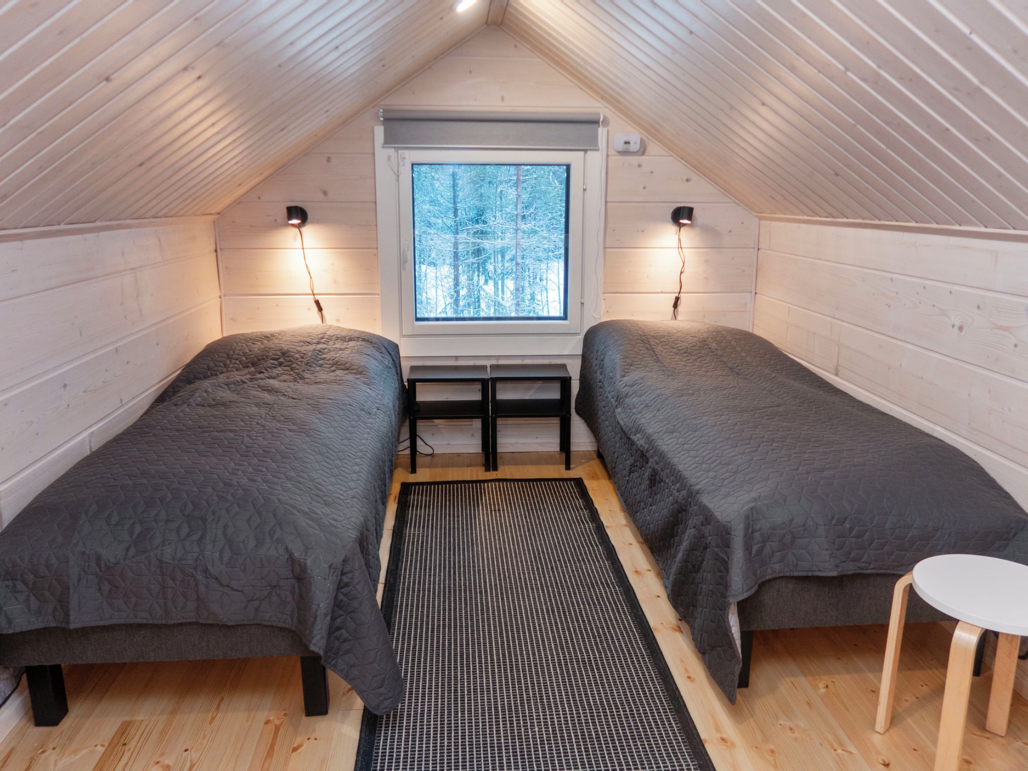 Une chambre confortable située dans les combles, avec deux lits, une petite table et une fenêtre donnant sur un paysage enneigé.