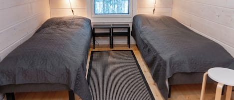 A cozy attic bedroom with two beds, a small table, and a window with a snowy view.