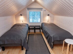 Quarto de sótão aconchegante com duas camas, uma mesinha e uma janela com vista para a neve.