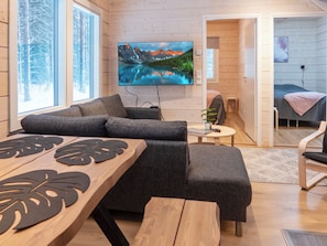 A cozy cabin interior with a large TV, a wooden dining table, and a comfortable seating area.