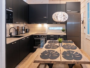 A modern kitchen with dark cabinets, stainless steel appliances, and a wooden dining table with leaf-patterned placemats. - Mäkitie 2 by Interhome (Kuusamo)