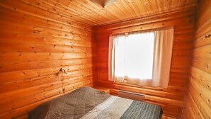 A wooden cabin room with a bed, a window with curtains, and a wall-mounted heater. - Mäkitupa 1 by Interhome (Kuusamo)