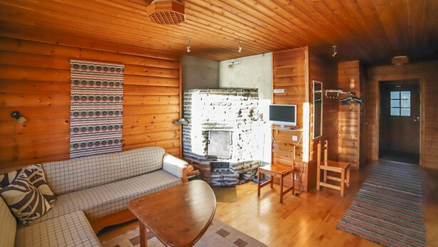 A cozy cabin interior with a wooden ceiling, a stone fireplace, a sofa, a small table, and a television on a stand. - Mäkitupa 1 by Interhome (Kuusamo)