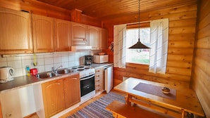 A compact kitchen with wooden cabinets, a stove, a sink, and a window with curtains. - Mäkitupa 1 by Interhome (Kuusamo)