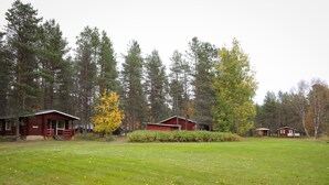 A campground with several cabins surrounded by tall trees and a grassy field. - Mäkitupa 1 by Interhome (Kuusamo)