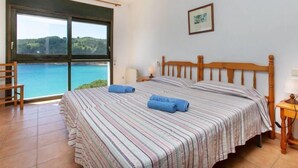 A bedroom with a large bed, a wooden headboard, a view of the sea, and a framed picture on the wall.