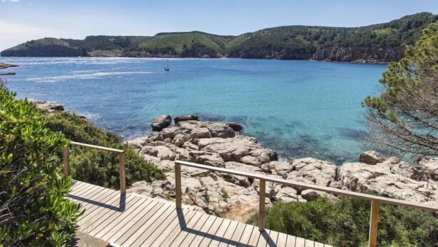 A coastal view with clear blue waters, rocky shoreline, and a wooden deck with railings. - Port del Rei I by Interhome (L'Escala)