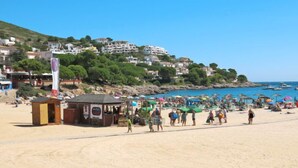 A beach with people walking, umbrellas, and a small wooden structure. - Port del Rei I by Interhome (L'Escala)