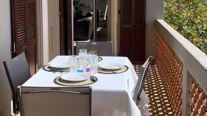 A balcony with a table set for dining, a chair, and a view of the cityscape. - Famous beaches 5 minutes from the house by car (Pianottoli-Caldarello)