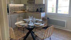 A dining area with a round table set for six, surrounded by wicker chairs, in a kitchen with white cabinets and a tiled backsplash. - Famous beaches 5 minutes from the house by car (Pianottoli-Caldarello)