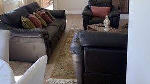 A living room with a black leather sofa set, a white armchair, and a patterned rug. There is a wall-mounted lamp and a framed picture on the wall. - Famous beaches 5 minutes from the house by car (Pianottoli-Caldarello)