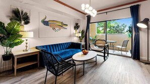 A modern living room with a blue sofa, a round coffee table, and a dining area with chairs. - Designer Corner Suite 3br/2ba - Disney & Universal (Orlando)