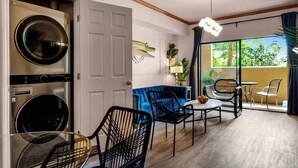A modern living room with a blue sofa, black chairs, a round table, and a large window with a view of greenery. - Designer Corner Suite 3br/2ba - Disney & Universal (Orlando)