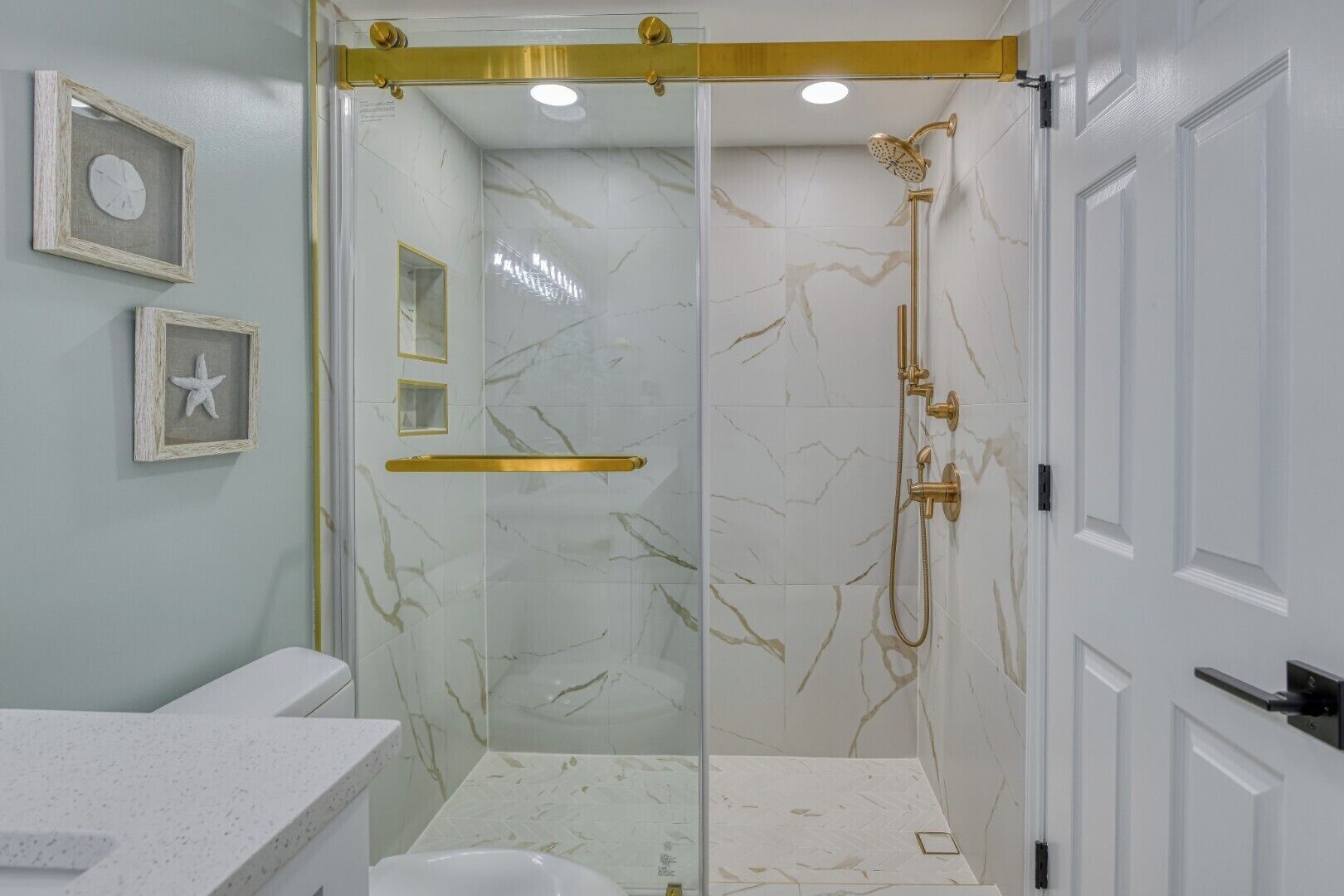 A bathroom with a glass-enclosed shower, marble walls, and a white sink.