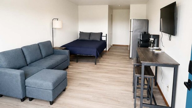 Un espace de vie moderne et compact comprenant un canapé, un lit, une kitchenette et un téléviseur à écran plat.