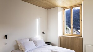 A bedroom with a bed, a window with a view of trees, and a wooden ceiling.