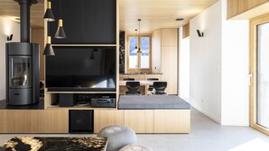 A modern living room with a large flat-screen TV, a wood-burning stove, and a dining area with a wooden table and chairs.