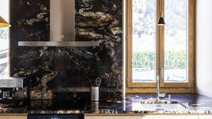 A modern kitchen with a black marble backsplash, stainless steel range hood, and a built-in coffee machine.