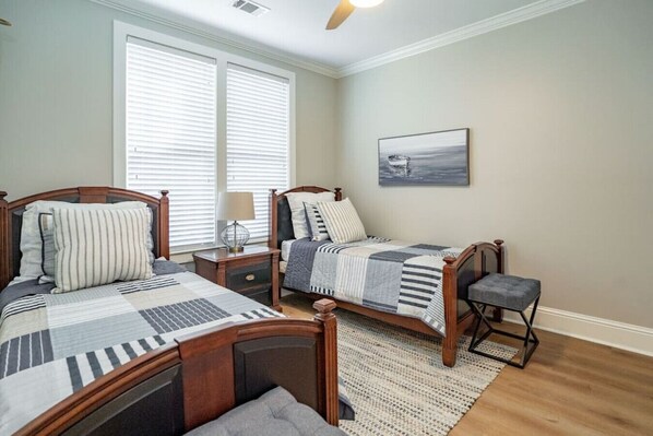 A bedroom with two wooden beds, a nightstand, a chair, and a large window with blinds. - Great Views, Great Location, Near Ritz, No Stairs (Greensboro)