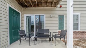 Une terrasse couverte avec une table et quatre chaises, une porte verte et un mur en briques.