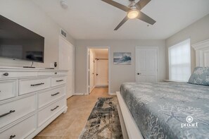 Une chambre à coucher comprenant un lit, un ventilateur de plafond, une commode et une porte donnant sur une autre pièce.