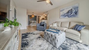 A modern living room with a beige sofa, a blue armchair, a tufted ottoman, and a large abstract painting on the wall. - Blue Dolphin - 5 minutes from the beach and close to everything! (Destin)