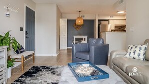A modern living room with a sofa, a coffee table with a board game, a bench, and a hanging light fixture. - Blue Dolphin - 5 minutes from the beach and close to everything! (Destin)
