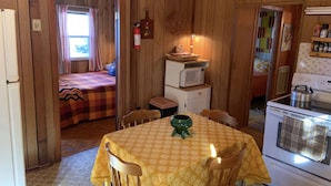 A cozy cabin interior with a dining table, chairs, a microwave, a stove, and a small kitchenette.