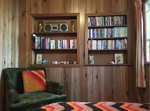 Um quarto aconchegante com uma poltrona verde, uma estante cheia de livros e um rádio em uma prateleira.