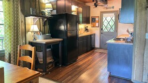 A compact kitchen with wooden cabinets, a black refrigerator, a small dining table, and a chair. - Lakefront cabin in quiet cove on Lake Hartwell (Hartwell)