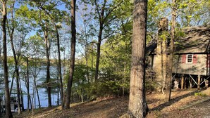 A rustic cabin with a wooden deck, surrounded by trees and a lake. - Lakefront cabin in quiet cove on Lake Hartwell (Hartwell)