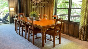 A wooden dining area with a table and chairs, a chandelier, and a view of greenery outside. - Lakefront cabin in quiet cove on Lake Hartwell (Hartwell)