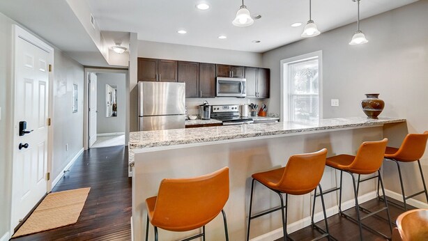 A modern kitchen with stainless steel appliances, a marble countertop, and a bar area with orange chairs. - Walkable to Oakley Square-Newly Renovated-King Bed (Cincinnati)