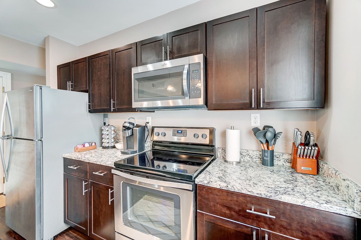 A modern kitchen with dark wood cabinets, stainless steel appliances, and granite countertops.