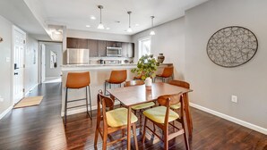 A modern kitchen with dark wood flooring, a dining area with a wooden table and chairs, and a kitchen island with seating. - Walkable to Oakley Square-Newly Renovated-King Bed (Cincinnati)