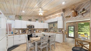 A modern kitchen with white cabinets, a central island, and a dining area with chairs. - Beautiful secluded setting on the Rainbow River surrounded by state forest (Dunnellon)