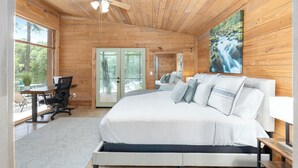 A bedroom with a large bed, a desk, and a chair. There is a window and a door leading to an outdoor area. - Beautiful secluded setting on the Rainbow River surrounded by state forest (Dunnellon)