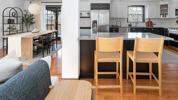 Une cuisine moderne dotée d’un îlot central, d’appareils électroménagers en acier inoxydable et d’un coin repas avec une table et des chaises en bois.