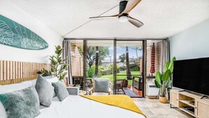 A modern bedroom with a bed, a TV, and a balcony with a view of the outdoors.