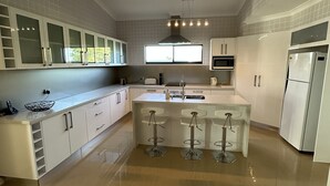 Una cocina moderna con armarios blancos, una isla central con taburetes de bar, horno empotrado y refrigerador.