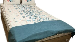 Een bed met een bloemenprint sprei, twee kussens met een blauw-roze ontwerp, en een blauwe deken.