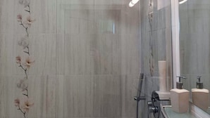 Een moderne badkamer met een douche, een wastafel met glazen ombouw en een spiegel.