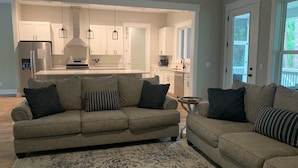 Una sala de estar moderna con un sofá color beige, un tapete estampado y una cocina al fondo.