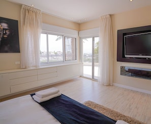 A modern bedroom with a large bed, a flat-screen TV, and a balcony with sliding doors.