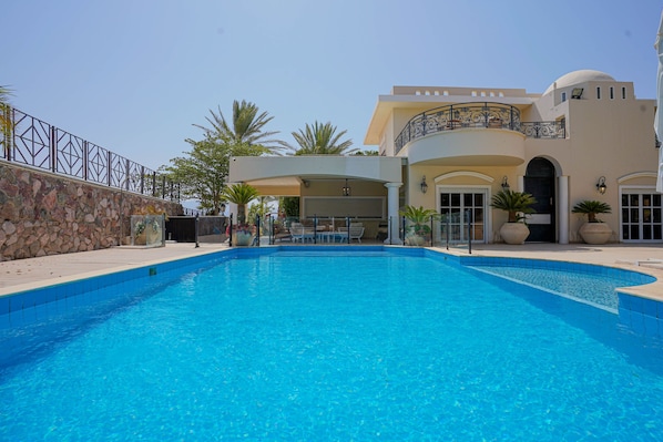 A swimming pool with a stone wall on one side and a building with a balcony on the other.
