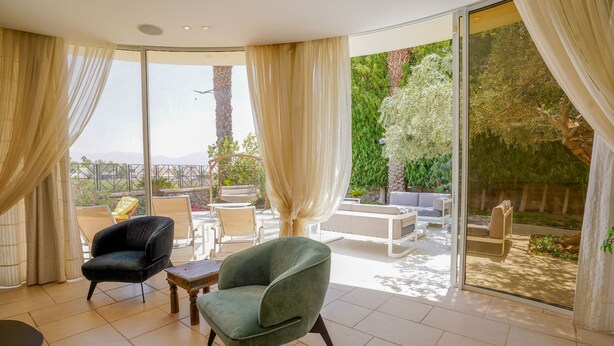 Una habitación amplia con un gran ventanal corredero que da a un patio exterior. En el interior, hay dos sillones y una pequeña mesa.